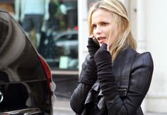 a woman talking on her cell phone while standing next to a parked car in front of a building