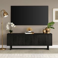 a living room with a large black tv on top of a wooden cabinet next to a lamp