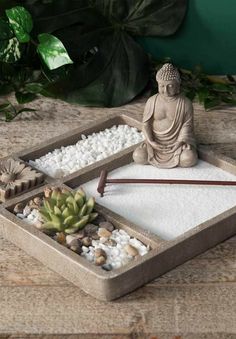 a small buddha statue sitting on top of a tray filled with rocks and gravel next to a succulent plant