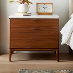 a nightstand with a clock on it next to a bed