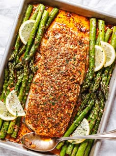 salmon and asparagus in a baking pan with lemon wedges on the side