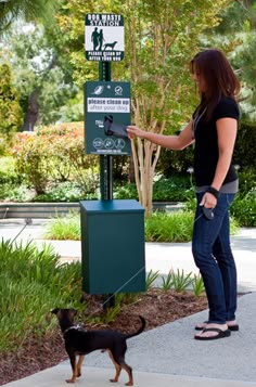 a woman standing next to a sign with a dog in front of it on a leash