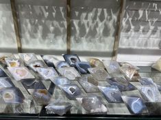 several different types of rocks on display in a glass case with shadows coming through the window