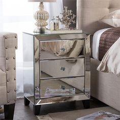 a mirrored night stand with two drawers and a lamp next to it on top of a bed