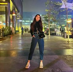 a woman standing in the middle of a street at night with her hand on her hip