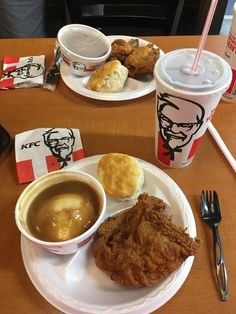 two plates with fried chicken, soup and coffee on a table next to sodas