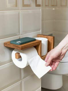 a person holding a roll of toilet paper in front of a wooden holder on the wall