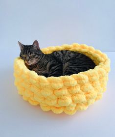 a cat laying in a yellow crochet bed on top of a white table