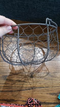 a person is holding a wire basket on a wooden table