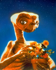 an alien holding a potted plant with flowers in it's hands and looking up at the sky