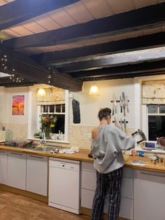 a woman standing at the counter in a kitchen with lots of clutter on it