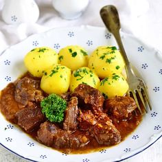 a white plate topped with meat and potatoes covered in gravy next to a fork