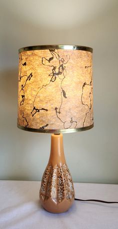 a lamp that is on top of a white table cloth with a brown vase underneath it