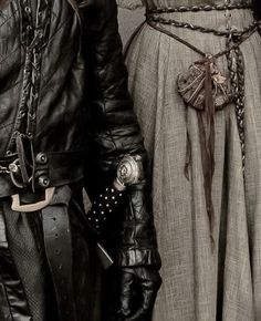 two people dressed in medieval clothing and holding hands with chains on their wrists, standing next to each other