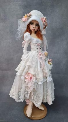 a doll wearing a white dress and bonnet with pink flowers on it's head