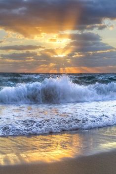 the sun is setting over the ocean with waves crashing in front of it and some clouds