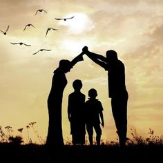 two adults and one child are silhouetted against the sunset with birds flying overhead over them