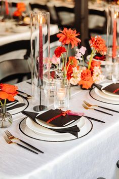 the table is set with black and white plates, silverware, and orange flowers