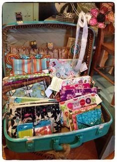 an open suitcase filled with lots of different types of fabric and fabrics on top of a wooden floor