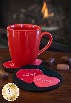 a red coffee cup sitting on top of a wooden table next to two coasters