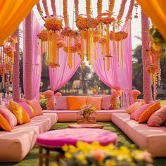 an outdoor wedding setup with pink and orange decorations on the couches, yellow drapes, and flowers