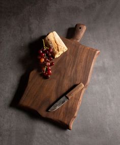 a wooden cutting board with grapes and cheese on it, next to a knife that has been cut in half