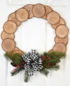 a wreath made out of logs and evergreen leaves with berries on the bottom is hung on a white door