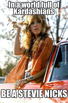 a woman leaning on the hood of a red car with her hand in her hair