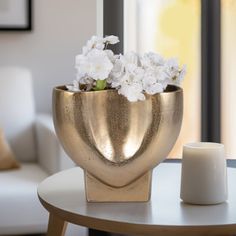 a gold vase with white flowers in it on a table next to a candle holder