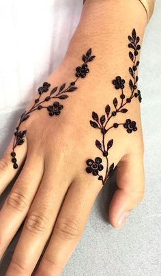 a woman's hand with black flowers and leaves on the left side of her arm