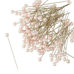 a bunch of pins with some white pearls on top of each other and one pink pin