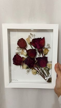 a person holding up a white frame with flowers in it