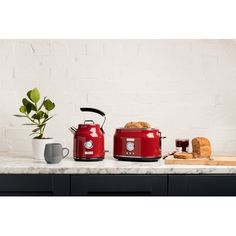 two red crock pots sitting on top of a counter next to a loaf of bread