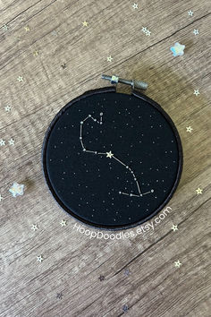 a black and white embroideryed zodiac sign on a wooden surface with stars around it