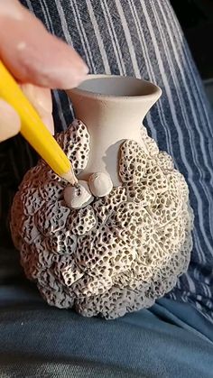 a person holding a yellow pencil in their left hand and a white vase with shells on it