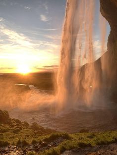 the sun is setting behind a waterfall with water shooting out from it's sides