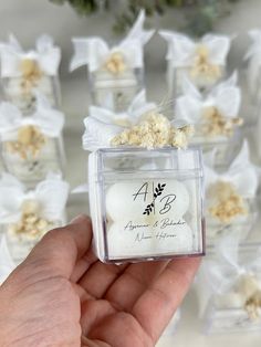 a person holding up a small glass box with flowers on it and the label in front of them