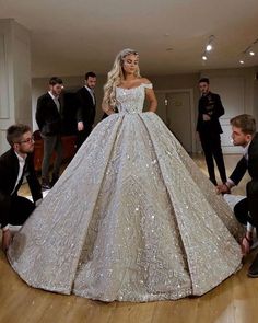 a woman in a wedding dress standing on the floor with other people around her and taking pictures