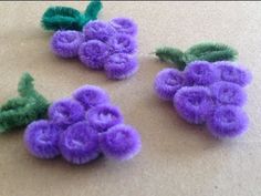 three small purple flowers with green stems on a counter top next to another flower that has been made out of felt