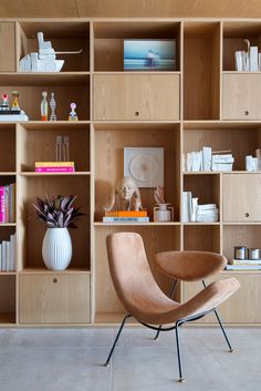 a chair sitting in front of a wooden book shelf filled with books and vases