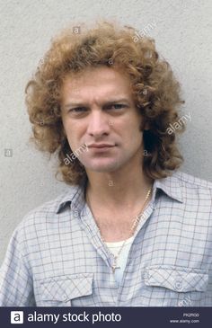 a young man with long curly hair wearing a blue shirt looking at the camera - stock image