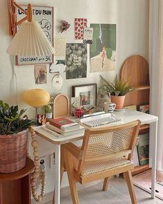 a desk with a lamp and some pictures on the wall next to potted plants