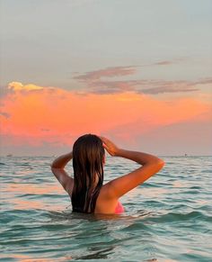 a woman standing in the ocean at sunset with her back to the camera, wearing a bathing suit