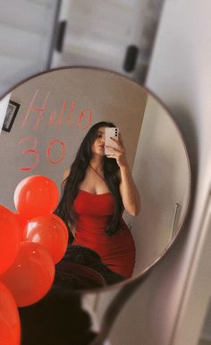 a woman in a red dress taking a selfie with her cell phone and balloons