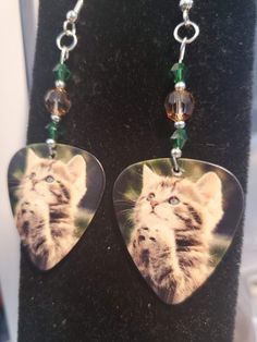 a pair of guitar pick earrings with a cat on it's face and green beads hanging from them