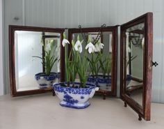 three mirrors with flowers in them sitting on a table next to each other and one is holding a potted plant