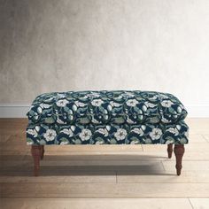 an upholstered footstool in front of a white wall and wooden floor