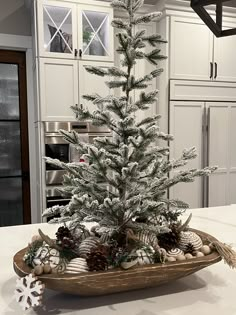 a white christmas tree in a wooden bowl on a counter top with snowflakes and pine cones