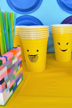 yellow cups with faces drawn on them are lined up in front of colorful paper straws