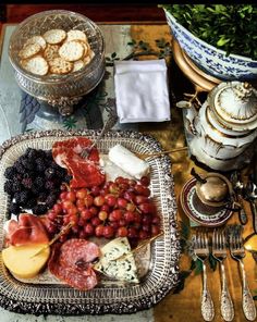 a platter of cheese, meats and fruit on a table with silverware